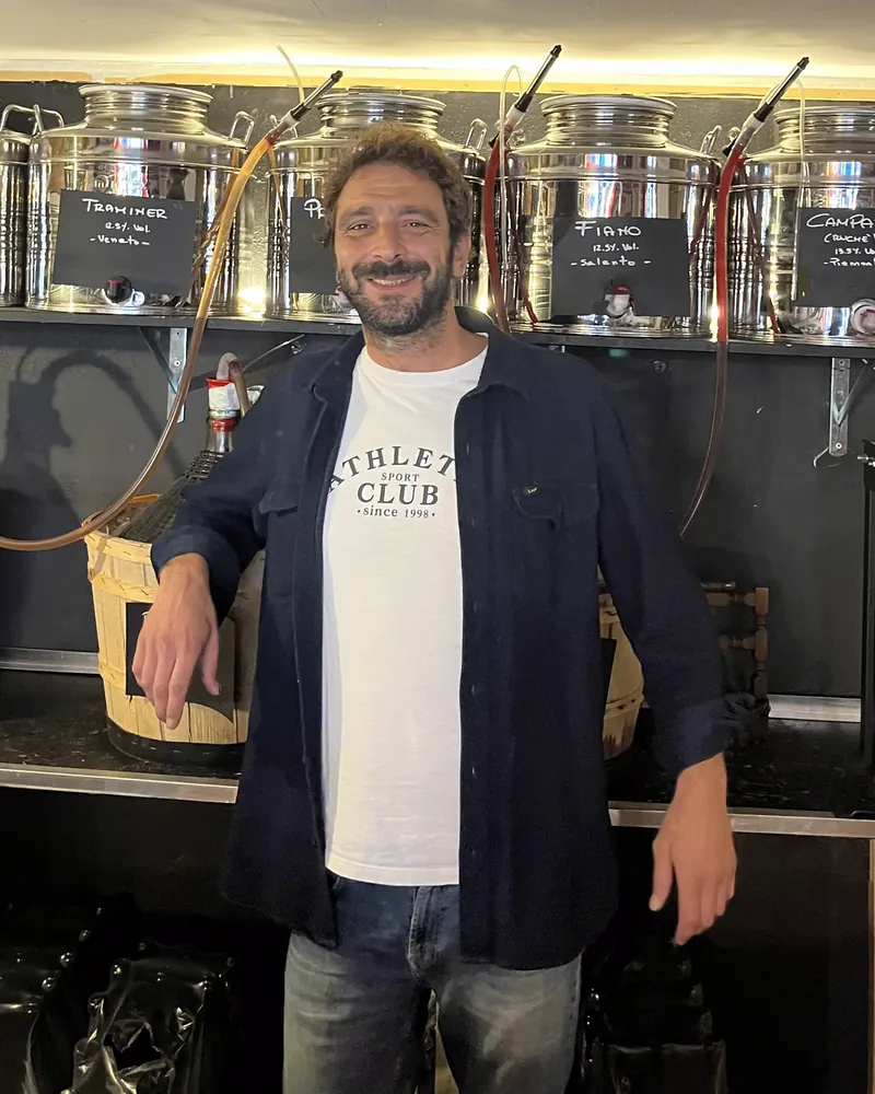 Giuseppe Cavallo sorridente davanti alla postazione del vino sfuso